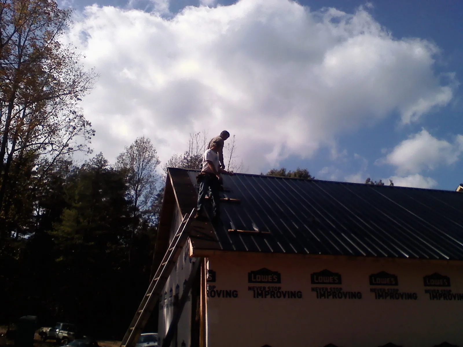 Roofer fastening dark metal panels high against a cloudy sky, from a Roof Inspection job in Leesburg